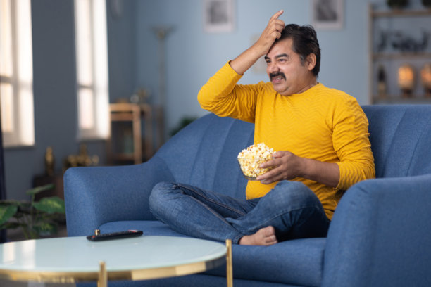 男人坐在家里的沙发上看电视的库存照片图片下载