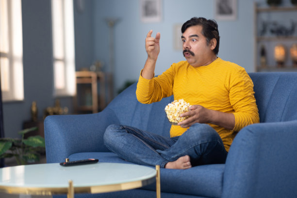 男人坐在家里的沙发上看电视的库存照片图片下载