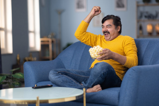 男人坐在家里的沙发上看电视的库存照片图片下载