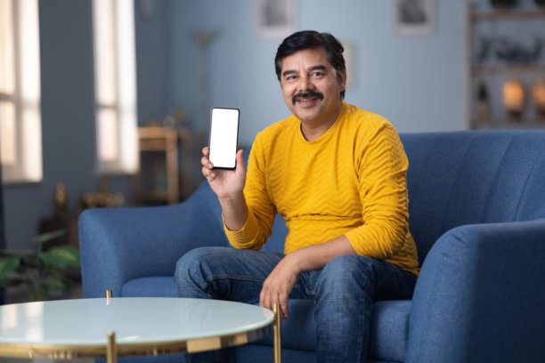 男人坐在家里的沙发上展示手机屏幕的库存照片图片下载