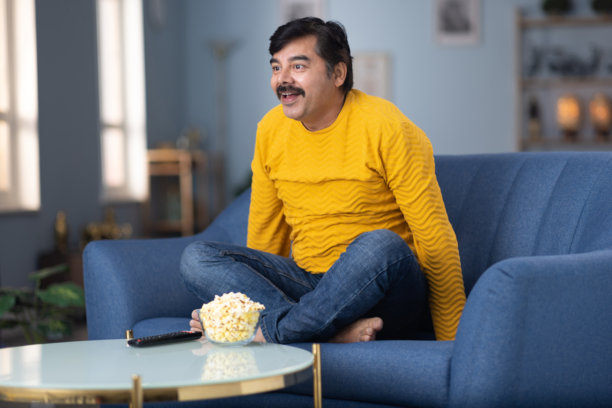 男人坐在家里的沙发上看电视的库存照片图片下载