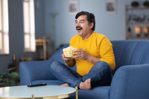 男人坐在家里的沙发上看电视的库存照片图片下载