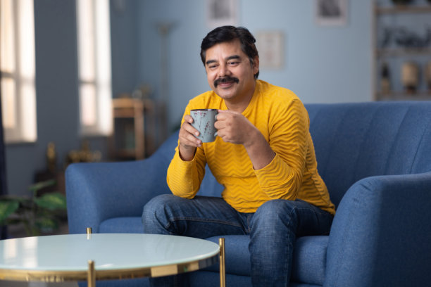 印度男子在家沙发上喝咖啡的照片图片下载