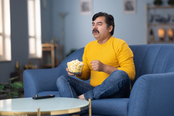 男人坐在家里的沙发上看电视的库存照片图片下载