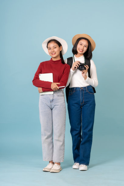 演播室里的主持人是两位亚洲女学生，穿着休闲服，正在探索一片美丽的森林，用相机拍摄风景，并将照片保存在笔记本电脑上。图片下载