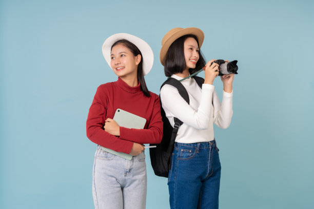 两名亚洲学生穿着休闲服装，走在古代遗址中，熟练地使用相机和笔记本电脑拍摄精彩的探索和知识照片。图片下载