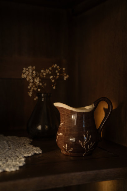木制橱柜架子上的陶瓷牛奶壶、碟子和装饰品，柔和温暖的阳光洒在上面。美学生活方式照片。图片下载