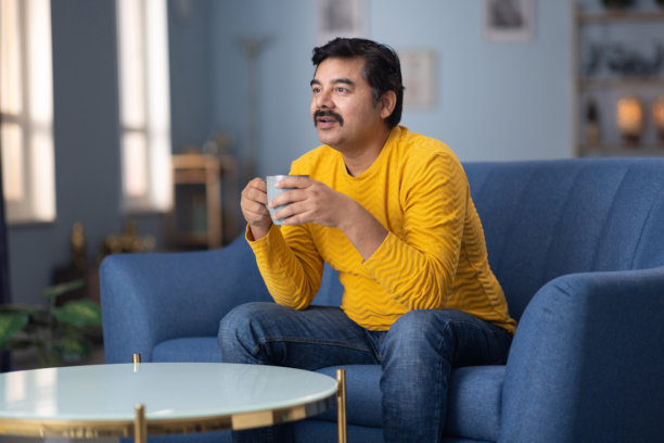 男人在家沙发上喝咖啡看电视的库存照片图片下载