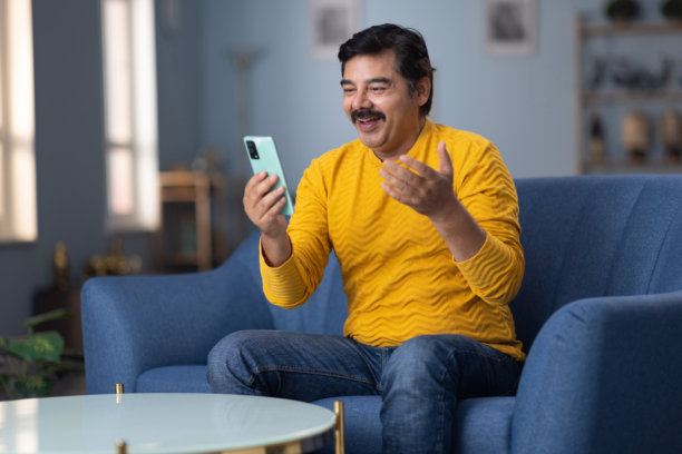 男人坐在家里的沙发上使用手机的库存照片图片下载