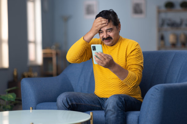 男人坐在家里的沙发上使用手机的库存照片图片下载