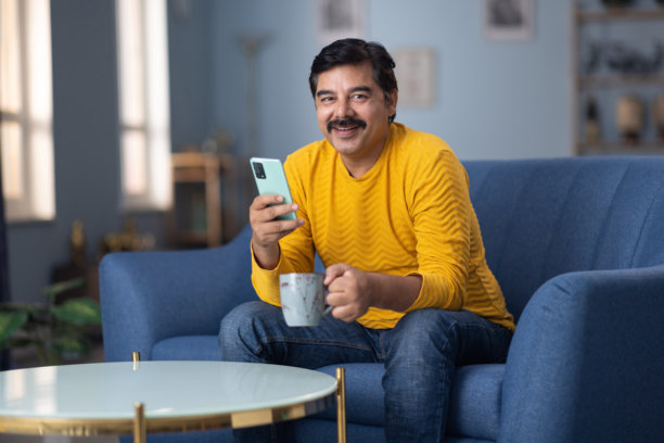 男人坐在家里的沙发上使用手机的库存照片图片下载