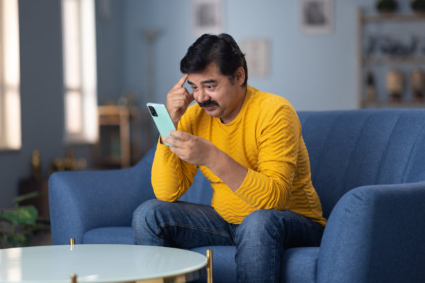 男人坐在家里的沙发上使用手机的库存照片图片下载