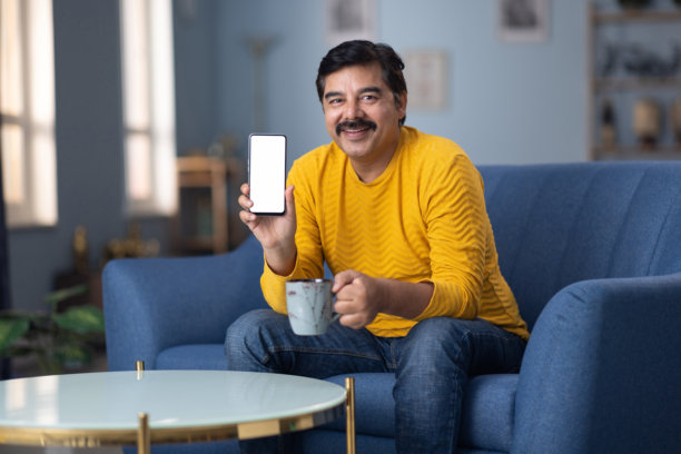 男人坐在家里的沙发上展示手机屏幕的库存照片图片下载