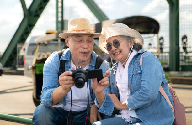一对老年夫妇在城市街道上散步后，放松地查看相机中的照片，背景是道路和桥梁结构。图片下载