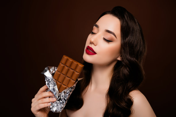 温柔迷人的女士在棕色背景下享用奶油巧克力棒糖果的照片图片下载