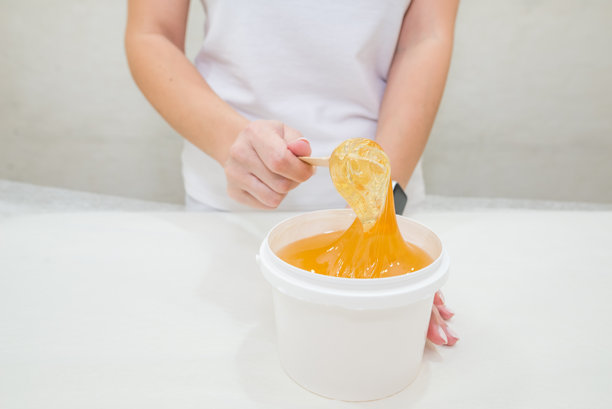 女性美容师手持一桶脱毛糖膏的特写照片。脱毛、去毛、蜡脱毛、糖脱毛的概念。图片下载