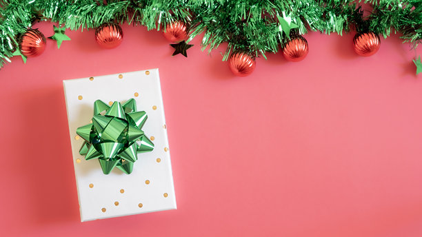 圣诞前夕概念。俯视照片展示了带有丝带蝴蝶结的礼品盒、绿色和红色的球饰、金色星星装饰物以及松枝，背景为孤立的红色，中央留有空白空间。图片下载
