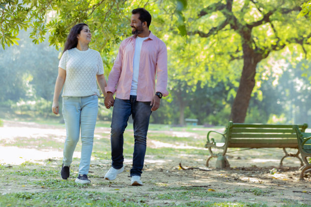 快乐的散步：一对情侣享受宁静的时刻，一张抓拍的照片，展示了一对幸福的情侣手挽手走过郁郁葱葱的公园。图片下载