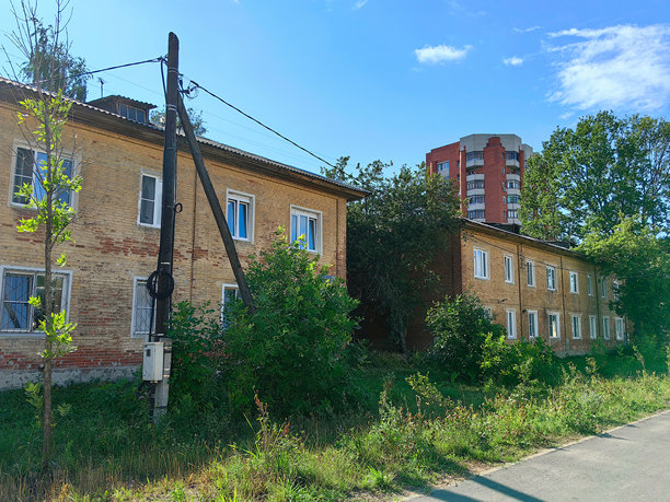 一条人行道和两座古老的两层橙砖住宅建筑，周围环绕着树木和高层建筑。俄罗斯。下诺夫哥罗德。兹奥尔科夫斯基街。2024年7月。照片图片下载