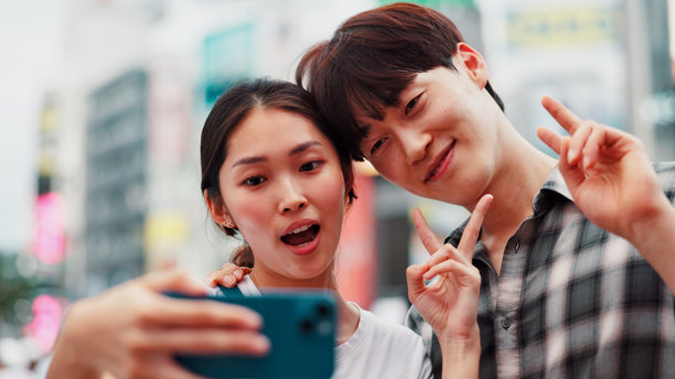日本城市中的情侣在街上合影，手势为和平符号，象征着亲密、爱情或旅游。日本女性与男性在城市中微笑的照片，适合假期、旅行或度假。图片下载