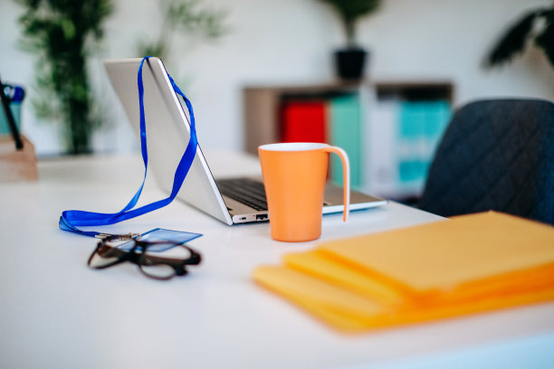 现代办公室的照片，没有人，笔记本电脑上挂着身份证，旁边有咖啡杯。图片下载