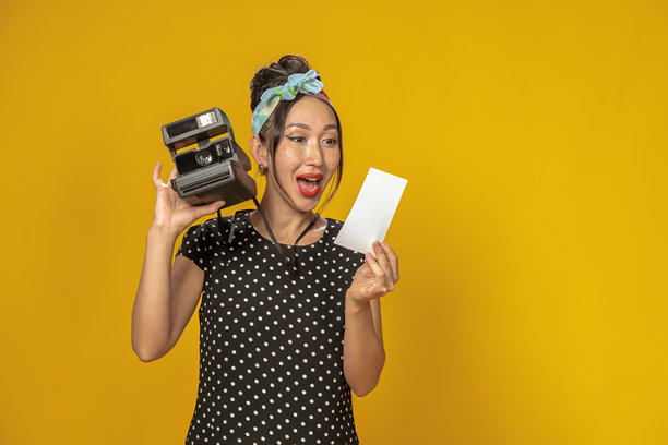 穿着复古风格的美丽亚洲女孩情感丰富地看着用即时相机拍摄的照片。背景干净，留有空白空间。图片下载