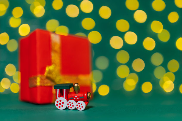 圣诞火车的照片，采用选择性对焦。圣诞装饰。圣诞背景。明亮的散景。绿色背景。一辆木质机车在绿色背景上。背景中有一个红色礼品盒。图片下载