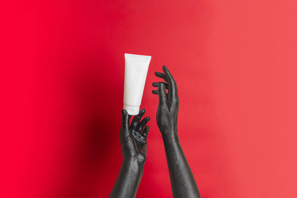 黑色涂漆的优雅手在她的肌肤上涂抹保湿化妆品，空白的管状奢华产品广告。适合您设计的图片。图片下载
