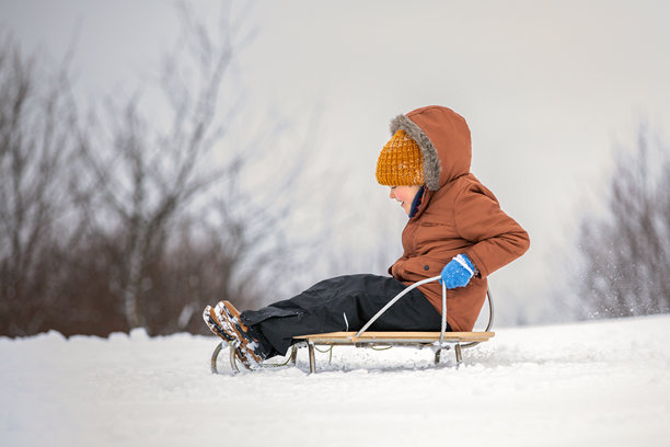 一个小男孩坐在木制雪橇上，被雪困住。头像图片图片下载