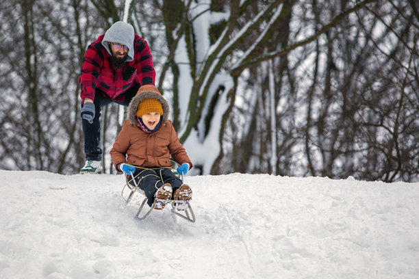 父亲和小儿子在公园里滑雪橇。冬季公园里的家庭滑雪。戴着可爱帽子的小男孩。横向照片图片下载