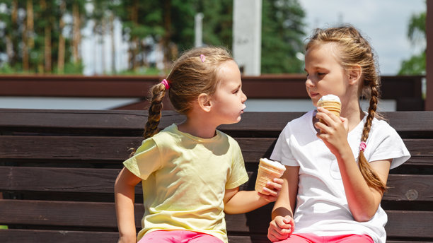 快乐的孩子们在户外一起吃冰淇淋。照片中快乐的女孩们坐在长椅上，面带微笑地看着镜头。图片下载
