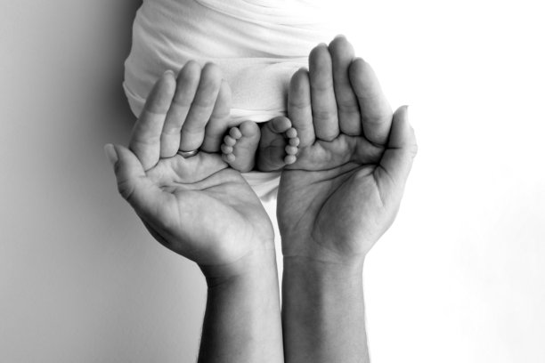 父母的手掌。一位父亲和母亲抱着包裹在毛毯中的新生儿的脚。父母手中握着新生儿的脚。黑白照片，展示脚、脚跟和脚趾。图片下载