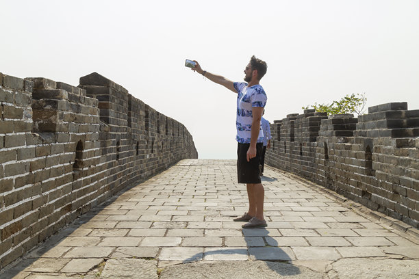 年轻的拉丁裔背包客男性游客在阳光明媚的夏日探索中国长城时，用智能手机拍摄令人惊叹的照片，享受着丰富的历史和壮丽的风景。图片下载