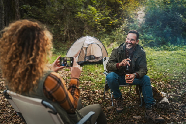 妻子在帐篷前拍摄丈夫享受时光的照片图片下载