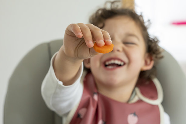 小女孩卷发，坐着穿着围嘴，享受着健康的食物，蔬菜和绿叶菜。儿童营养、关爱和健康生活方式的概念。婴儿主导的辅食。图片下载