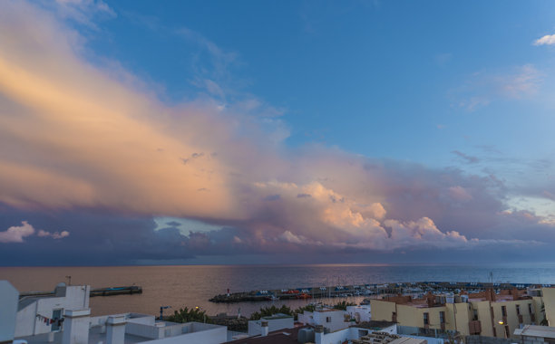 西班牙加那利群岛富埃特文图拉岛格兰塔哈尔镇的全景。照片展示了沿着沙滩排列的五彩缤纷的建筑，温柔的海浪在晴朗的蓝天下轻轻拍打着海岸。图片下载