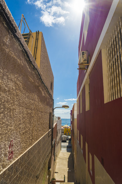 西班牙加那利群岛富埃特文图拉岛格兰塔哈尔镇的全景。照片展示了沿着沙滩排列的五彩缤纷的建筑，温柔的海浪在晴朗的蓝天下轻轻拍打着海岸。图片下载