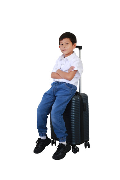 坐在行李箱上的亚洲小男孩，双臂交叉，姿势放松，背景为白色。儿童与旅行的概念。全身照片，带有抠图路径。图片下载