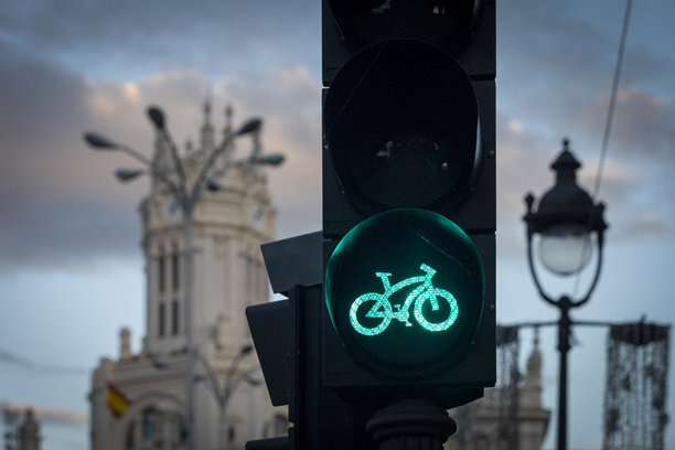 这张图片展示了马德里街道上的绿色自行车交通信号灯，背景是标志性的西贝莱斯宫，西班牙。图片下载