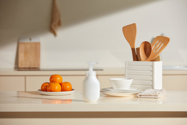 在阳光明媚的厨房背景下的宣传照片。一个空白标签的泵瓶放置在厨房岛的中央，周围是一些乡村风格的厨房用具和一个橙色盘子。图片下载
