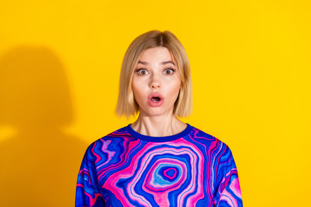 漂亮年轻女孩的照片肖像，惊恐而惊讶的表情，穿着时尚多彩的蓝色服装，背景为黄色。图片下载