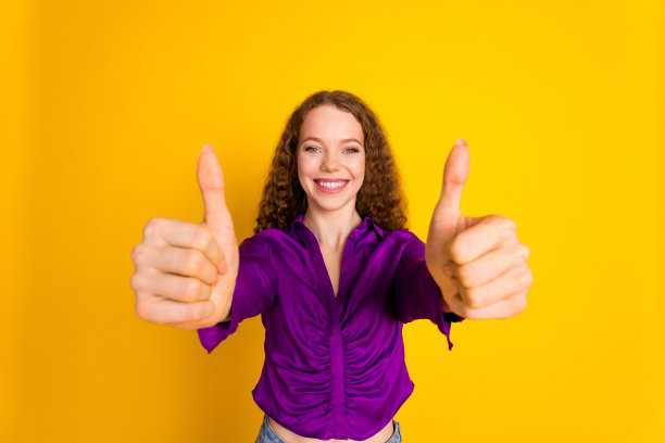 穿着时尚紫色衣服的迷人年轻女性在黄色背景下竖起大拇指的照片肖像图片下载
