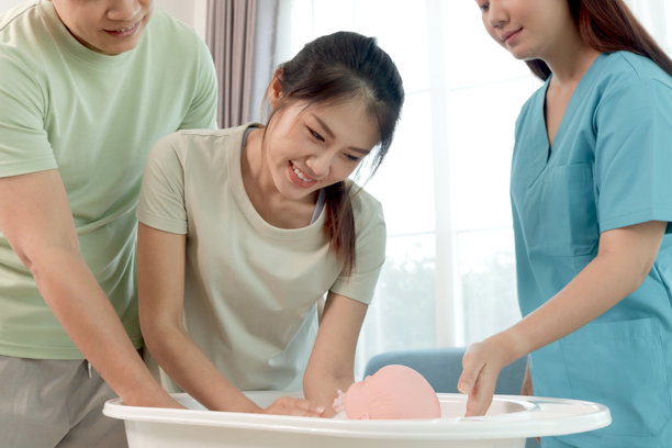 快乐的亚洲夫妇在女性护士的指导下学习给婴儿洗澡。孕妇和她的丈夫正在用玩偶练习给婴儿洗澡。孕妈妈正在接受医务人员的建议。图片下载