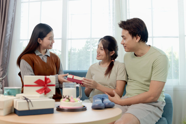 快乐的亚洲家庭夫妇在家中，漂亮的孕妇与丈夫和朋友们坐在沙发上庆祝婴儿洗礼派对。孕妈妈在派对上收到朋友送的礼物盒。图片下载