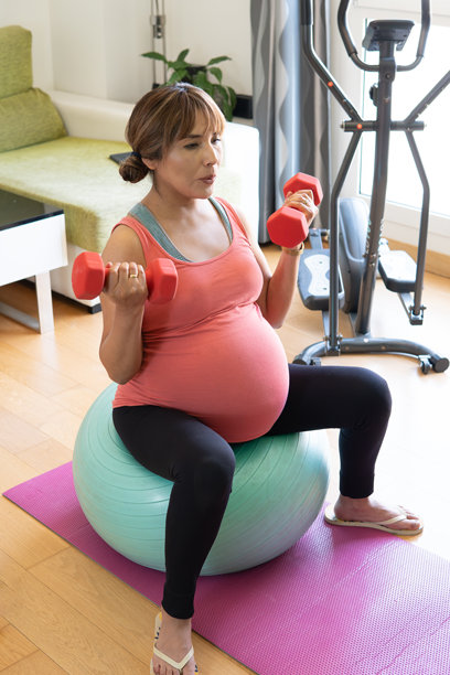 一位孕妇坐在瑜伽球上进行带重物的产前锻炼。准备分娩。概念：怀孕、母性、生育、产前锻炼。图片下载