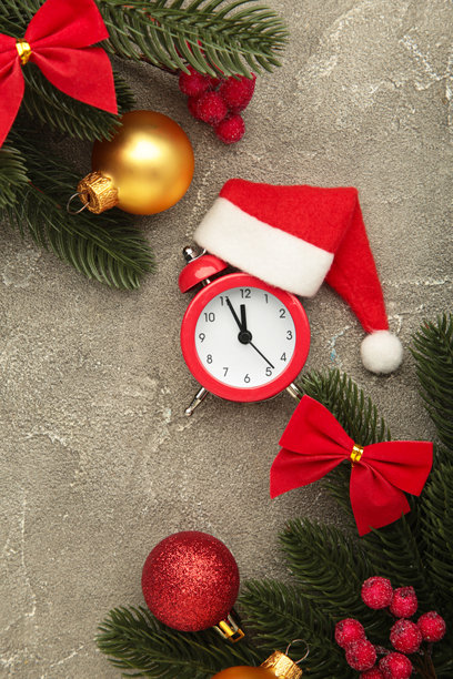 带圣诞帽的闹钟与白色冷杉树在灰色背景上。竖版照片图片下载