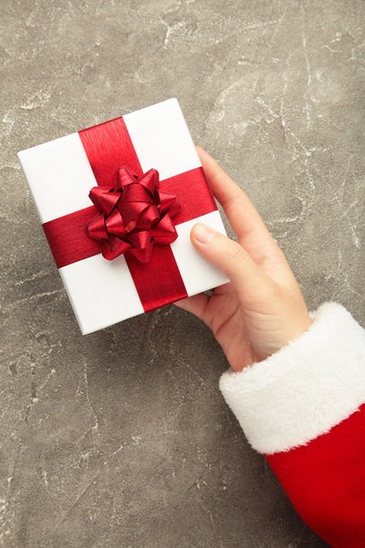 圣诞快乐概念，圣诞老人手握白色礼品盒的俯视图，灰色背景。竖版照片图片下载