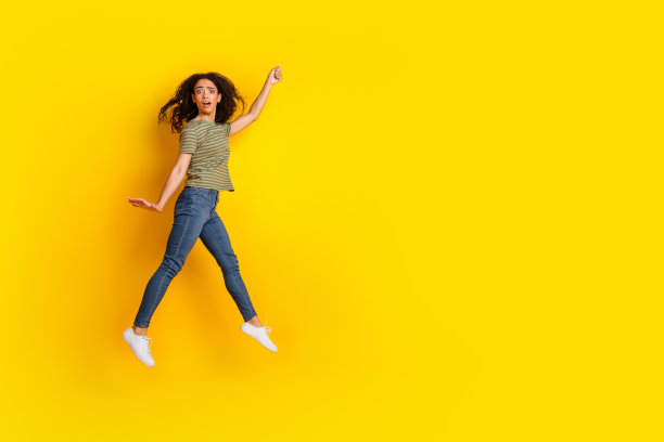 穿着条纹T恤和牛仔裤的惊讶女孩在空旷的黄色背景上飞手抓住物体的全身照片图片下载