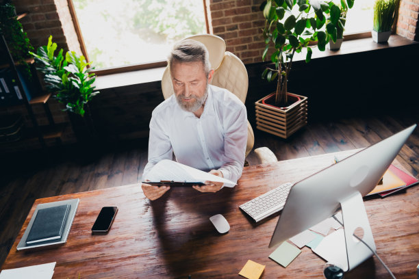 成功的专业男士穿着衬衫在室内工作站阅读文件报告合同的照片图片下载