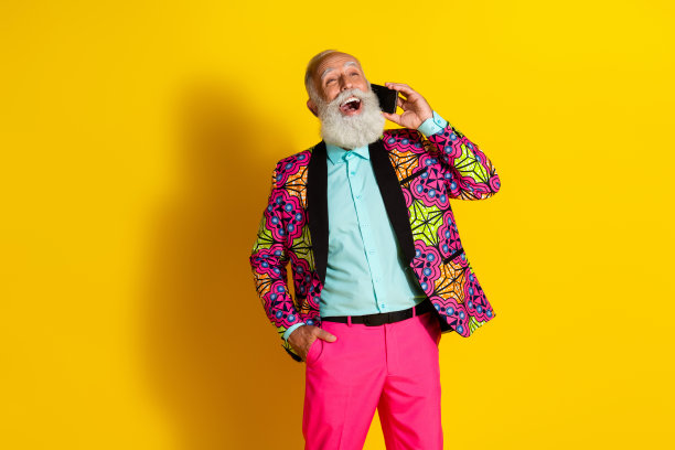 穿着时尚多彩华丽服装的和蔼老年男性在黄色背景下打电话的肖像照片图片下载